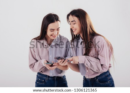 Look at this funny picture. Two sisters twins standing and posing in the studio with white background.