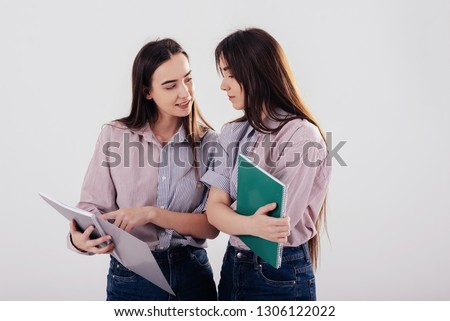 Interesting information in the notepads. Two sisters twins standing and posing in the studio with white background.