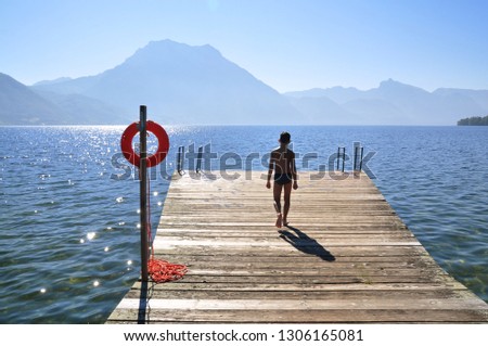 Silhouette of a boy walking on the wooden pierce at the lake in the mountains in Austria. Orange lifebuoy with a rope - safety on water concept