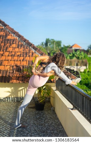Young woman practicing yoga, advanced yoga outside. 
Yoga on the roof at dawn overlooking the palm trees and rice fields of Bali.