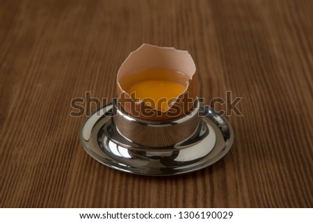 Broken in the middle a raw chicken egg with yolk and protein, on a round steel pedestal/ stand, which is located on a brown wooden table, side view.