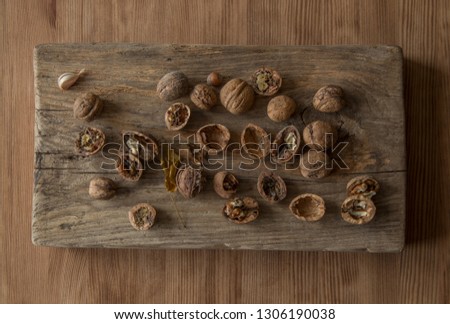 Walnuts, whole, broken, halves, acorn, garlic clove, yellow leaf, which are on the old wooden cutting board, which lies on the new wooden table.
