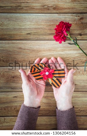 Concept background of May 9 russian holiday Victory Day. Old woman holding in hands a red carnation and St. George's ribbon. Flat lay