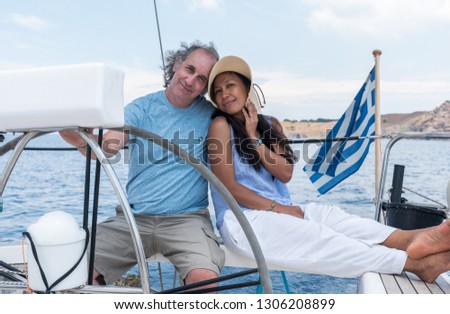 Man and woman with hat  in cockpit of sailboat with Greek flag