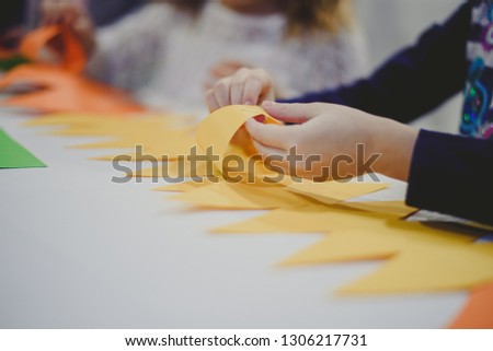 Little kids hands making decorations out of paper on a white table