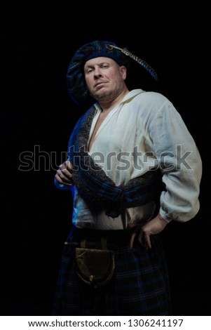Emotional Man with a beard in a blue checkered Scottish costume posing on a black background