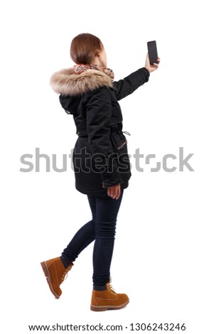 Back view woman in winter jacket who makes selfie with a smartphone. girl  watching. Rear view people collection.  backside view of person.  