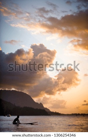 Scenic view of a surfer waiting on a calm sea with coastline and clouds lit by a sunrise.