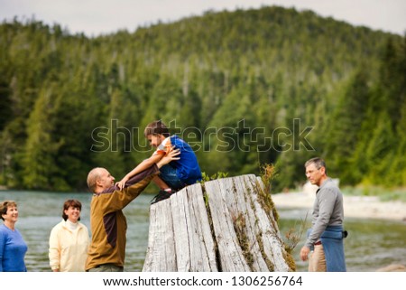 Smiling man holding his son on top of the stump of a dead tree.