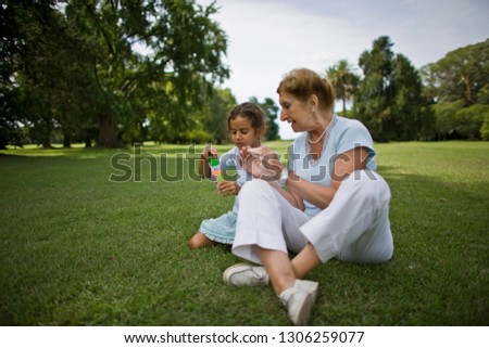 Senior woman talking to her young granddaughter while sitting on the grass outside.