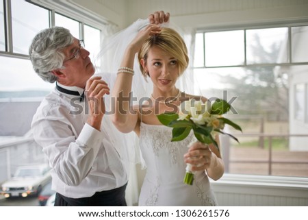 Young bride getting help to attach her veil while holding her bouquet inside a room.