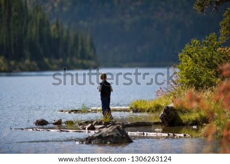 Young boy standing on a rock at the edge of a river.