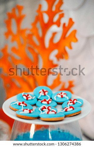 Big white plate with a lot of ginger bread cookies with bright blue icing and sea time d cor. Orange wooden corals on the background.
