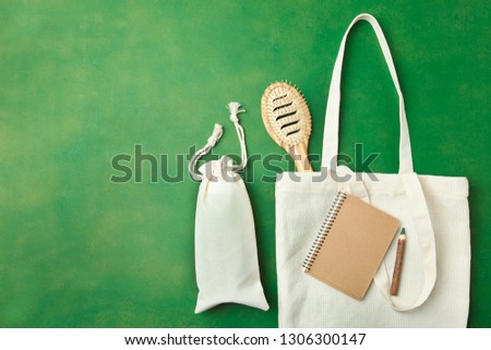 Two white eco bags of flax, bamboo hairbrush and craft notebook on green background. Flat lay, copy space. Environmentally friendly materials.