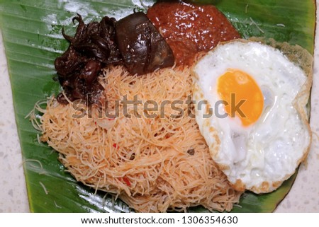 A picture of fried rice noodle with sunrise egg, "sambal sotong" and shrimp sauce for breakfast in banana leaf. Malaysian love to have heavy breakfast.