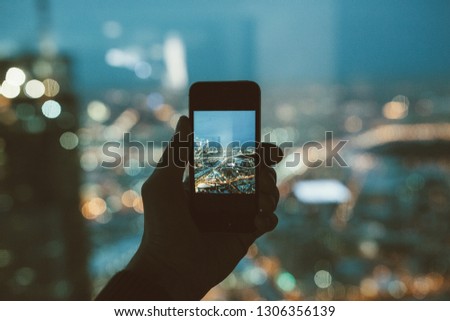 man hand takes photo of night city from high floor on phone through glass window