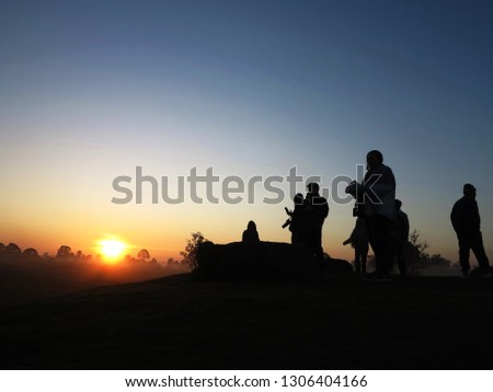 A group of tourists enjoyed to watch sunrise in the early morning with doing some activities in silhouette .