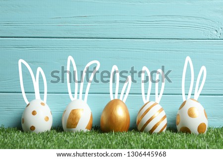 Decorated Easter eggs and cute bunny's ears on green grass against wooden background. Space for text 