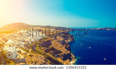 View of the Santorini Island with a smooth sea blue surface and steep shores with light struck place on the left