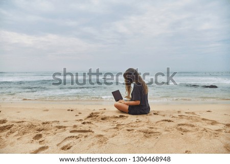 Young girl working at the computer on the beach. The freelancer working on the beach. Beach of the Indian ocean. Sri-lanka.