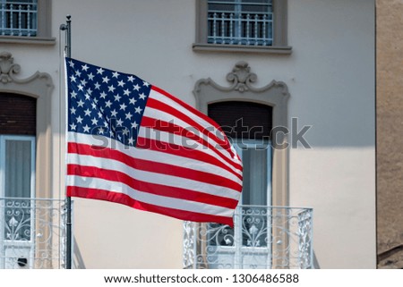 United States national flag waving in front of traditional retro italian houses  on a sunny summer day on the coast of the famous lake Como. Patriotic feeling and recognition, travel and tourism.