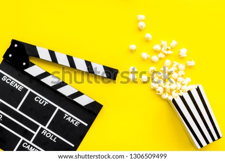 Movie premiere concept. Clapperboard and popcorn on yellow background top view space for text