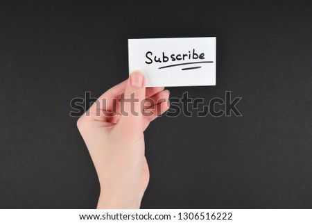 Subscribe text on a card in woman hand  on a black background.