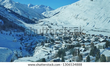 Beautiful winter snowy alpine scene from Andamatt, Switzerland. Snow covered roof tops under blue skies with the high alps marching in to the distance.