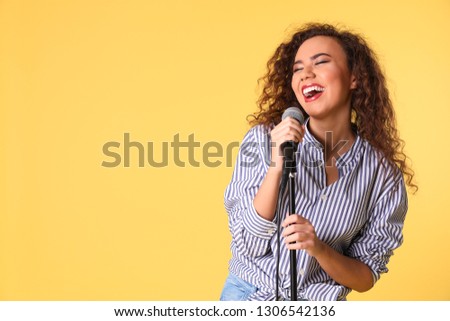 Portrait of curly African-American woman singing in microphone on color background. Space for text