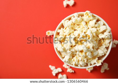 Fresh tasty popcorn and cup on color background, top view with space for text. Cinema snack