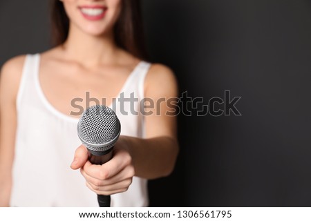 Young woman holding microphone on dark background, closeup view with space for text