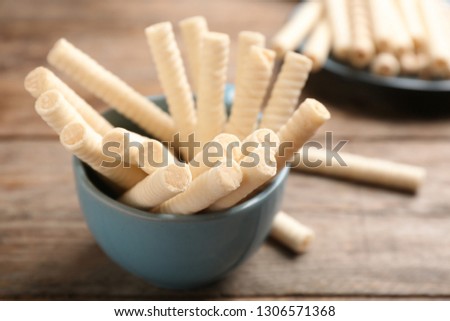 Bowl with delicious wafer rolls on wooden table, closeup. Sweet food