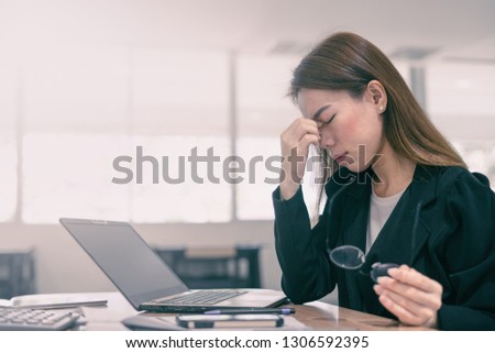 Tired and stressed asian business woman closed eyes massaging nose and sitting at desk in front of laptop at office background Royalty-Free Stock Photo #1306592395