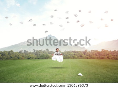 Young little boy keeping eyes closed and looking concentrated while meditating on cloud in the air with beautiful and breathtaking landscape on background.