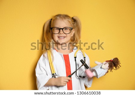 Cute child imagining herself as doctor while playing with reflex hammer and doll on color background