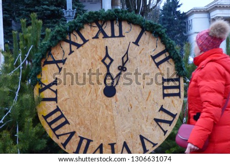 cardboard clock near the Christmas tree in the square and a girl in a red jacket