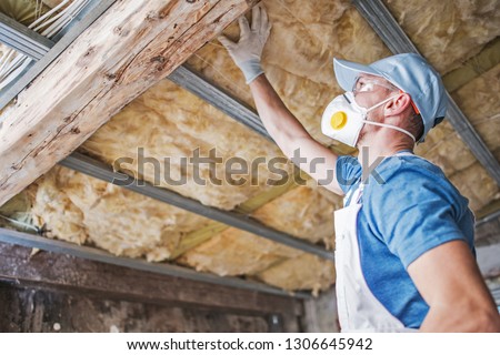 Old Roof Insulation. Caucasian Construction Worker in His 30s Inspecting Aged Roof and Mineral Wool Insulator. Royalty-Free Stock Photo #1306645942