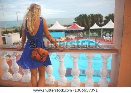 Carefree happy girl in dress standing at the balcony and looking at sea and resort with pool. Varadero, Cuba