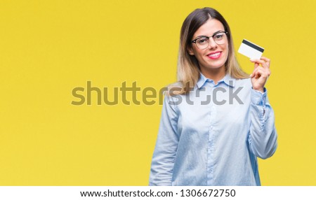 Young beautiful business woman holding credit card over isolated background with a happy face standing and smiling with a confident smile showing teeth