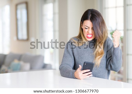 Young beautiful woman using smartphone at home annoyed and frustrated shouting with anger, crazy and yelling with raised hand, anger concept