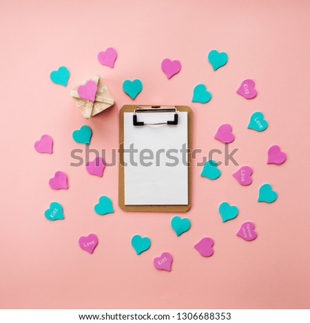 Top view composition of notebook with empty white pages surrounded by heart shaped confetti on pink background. Greetings on Valentine's day. Space for text or design. 