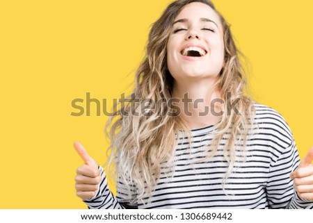 Beautiful young blonde woman wearing stripes sweater over isolated background success sign doing positive gesture with hand, thumbs up smiling and happy. Looking at the camera with cheerful expression