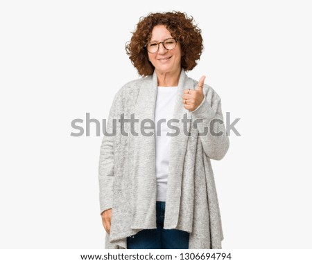 Beautiful middle ager senior woman wearing jacket and glasses over isolated background doing happy thumbs up gesture with hand. Approving expression looking at the camera showing success.