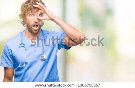 Handsome hispanic surgeon doctor man over isolated background doing ok gesture shocked with surprised face, eye looking through fingers. Unbelieving expression.