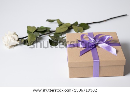 Gift box with purple ribbon and white rose. Valentines day or birthday gift.
