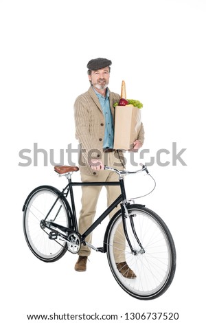 cheerful pensioner smiling whole hoding paper bag with groceries and bicycle isolated on white
