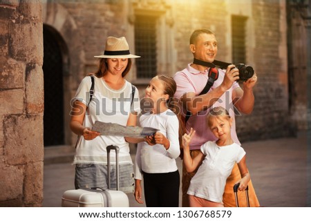 Pleasant tourist family using map and taking photo of city while strolling with camera and phone 