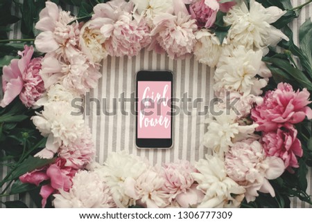 Girl Power text sign on phone screen and peonies frame flat lay on rustic table cloth.  Happy Women's Day stylish floral greeting card. International womens day