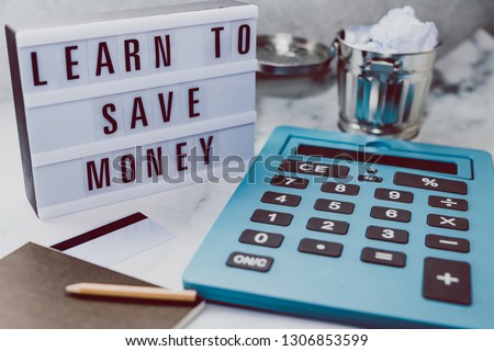 lightbox with Learn to save money message next to payment card calculator and stationery on marble desk, concept of learning to spend less and refrain from excessive shopping