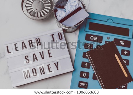 lightbox with Learn to save money message with payment card in the trash and stationery on marble desk, concept of learning to spend less and refrain from excessive shopping